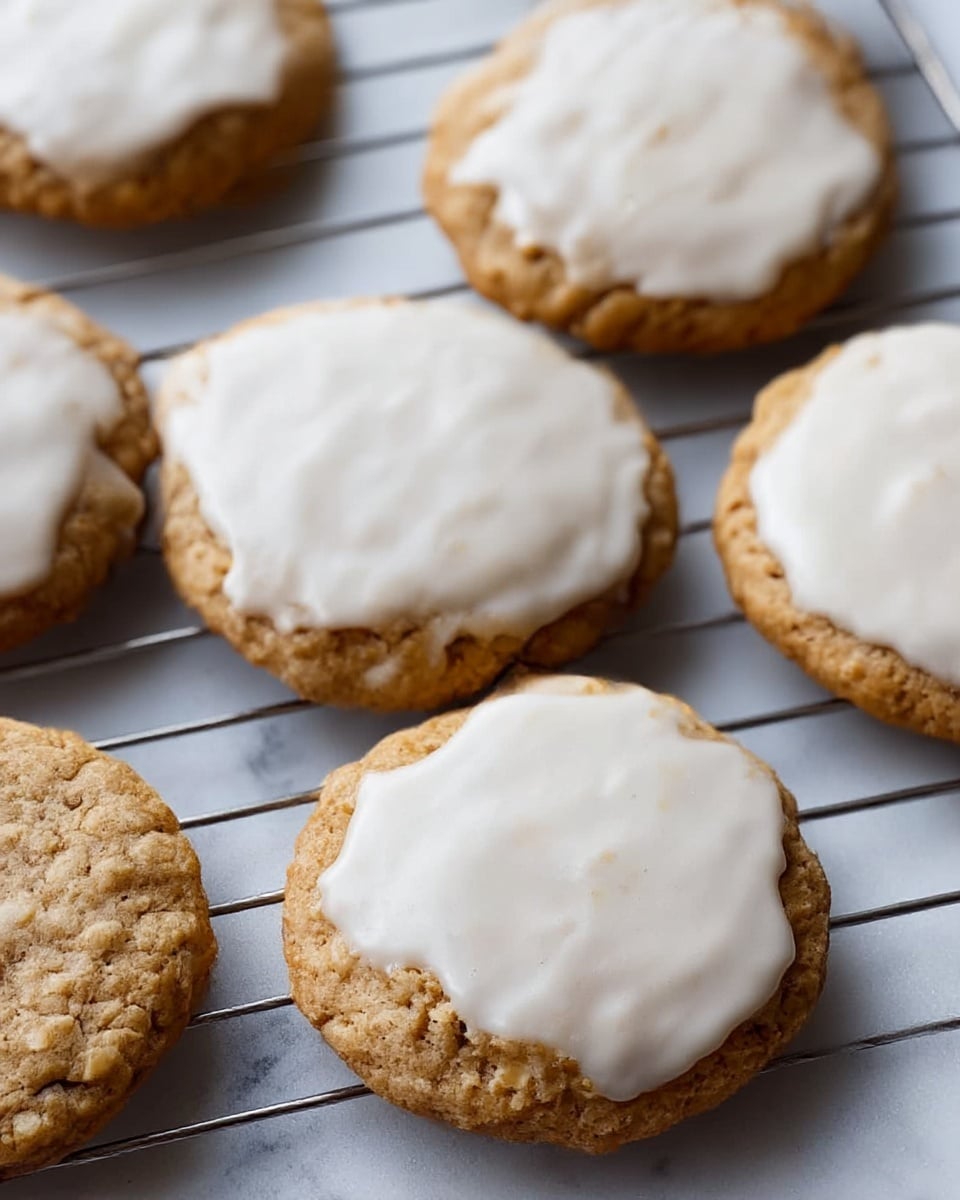 The image shows six round cookies on a metal cooling rack, each topped with a smooth, white icing layer covering the rough, brown cookie base. The cookies have a slightly cracked texture under the icing, giving a homemade, fresh-baked look. The cooling rack sits on a white marbled surface, adding a clean and elegant background to the warm, soft colors of the cookies. The close-up view highlights the icing's soft shine and the crumbly cookie edges. photo taken with an iphone --ar 4:5 --v 7