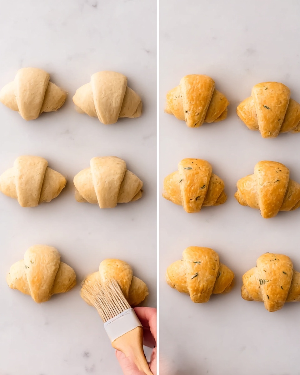 Pizza Crescent Rolls with Pepperoni and Mozzarella Recipe 5 The image shows eight small crescent rolls arranged in two columns on a white marbled surface. On the left side, three unbaked rolls with a pale dough color are placed vertically, while a pastry brush held by a woman's hand is gently applying a glaze to one roll. On the right side, five baked crescent rolls have a warm golden-brown color with small herbs visible in the dough, and the same brush and woman's hand are positioned near the bottom left roll. The texture of the dough looks soft and slightly flaky. photo taken with an iphone --ar 4:5 --v 7