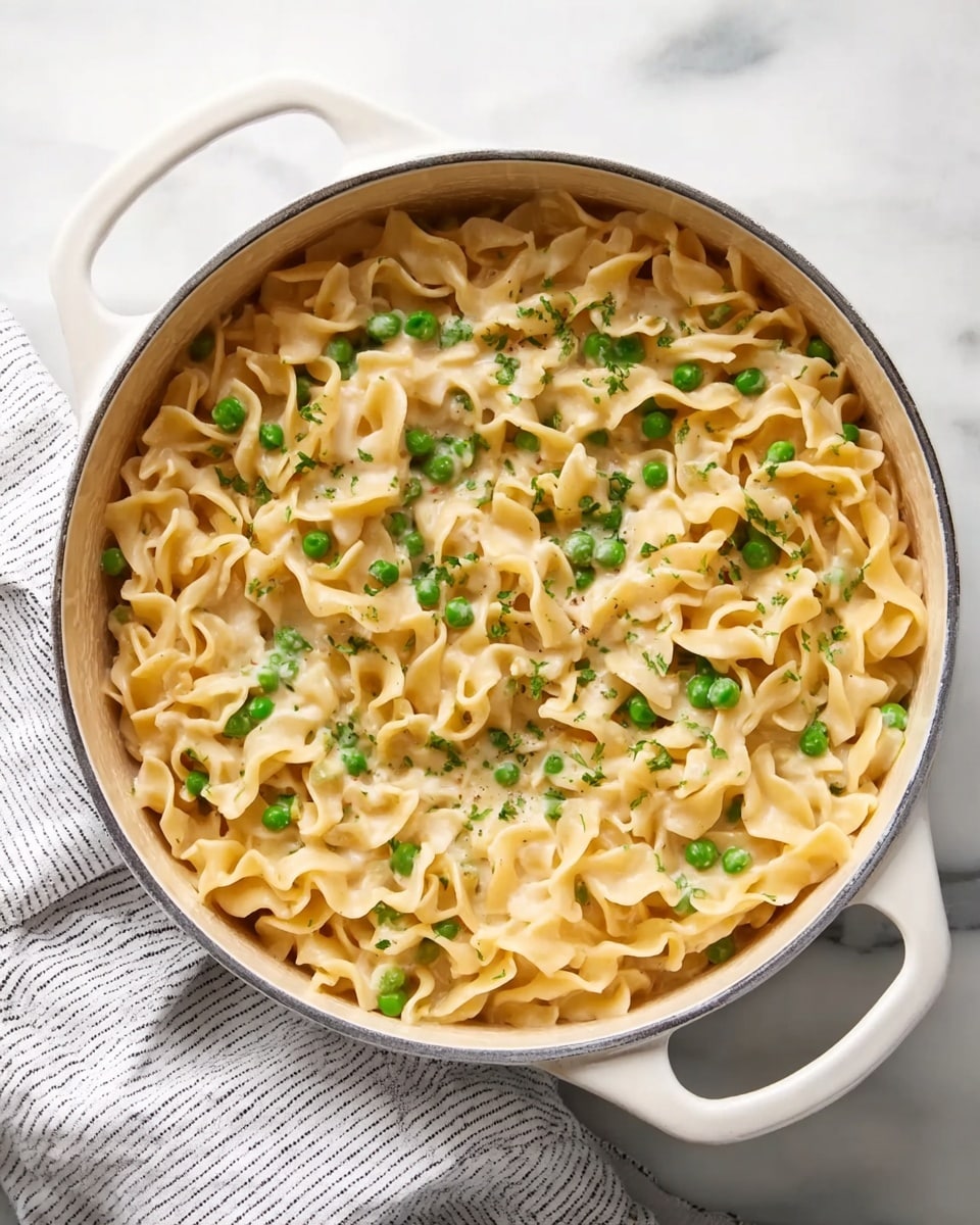 The image shows a white pot filled with creamy cooked pasta mixed with green peas. The pasta is wavy and light yellow, thickly coated with a smooth, light-colored creamy sauce. The green peas are scattered evenly throughout the pasta, adding bright spots of color. The pot is placed on a white marbled surface with a white and gray striped cloth partly under it. The pot has two handles and the overall look is cozy and inviting. photo taken with an iphone --ar 4:5 --v 7