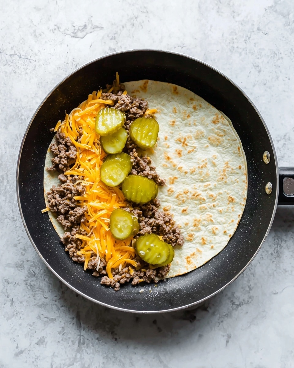 A black frying pan with a white tortilla inside takes up most of the frame, placed on a white marbled surface. On the left half of the tortilla, there is a layer of shredded orange cheddar cheese topped by crumbled cooked ground beef. Five bright green pickle slices are scattered evenly on top of the beef, giving the dish a fresh contrast. The right half of the tortilla remains plain, showing the light, slightly textured surface of the tortilla. The lighting highlights the colors and textures clearly, creating an appetizing look. photo taken with an iphone --ar 4:5 --v 7