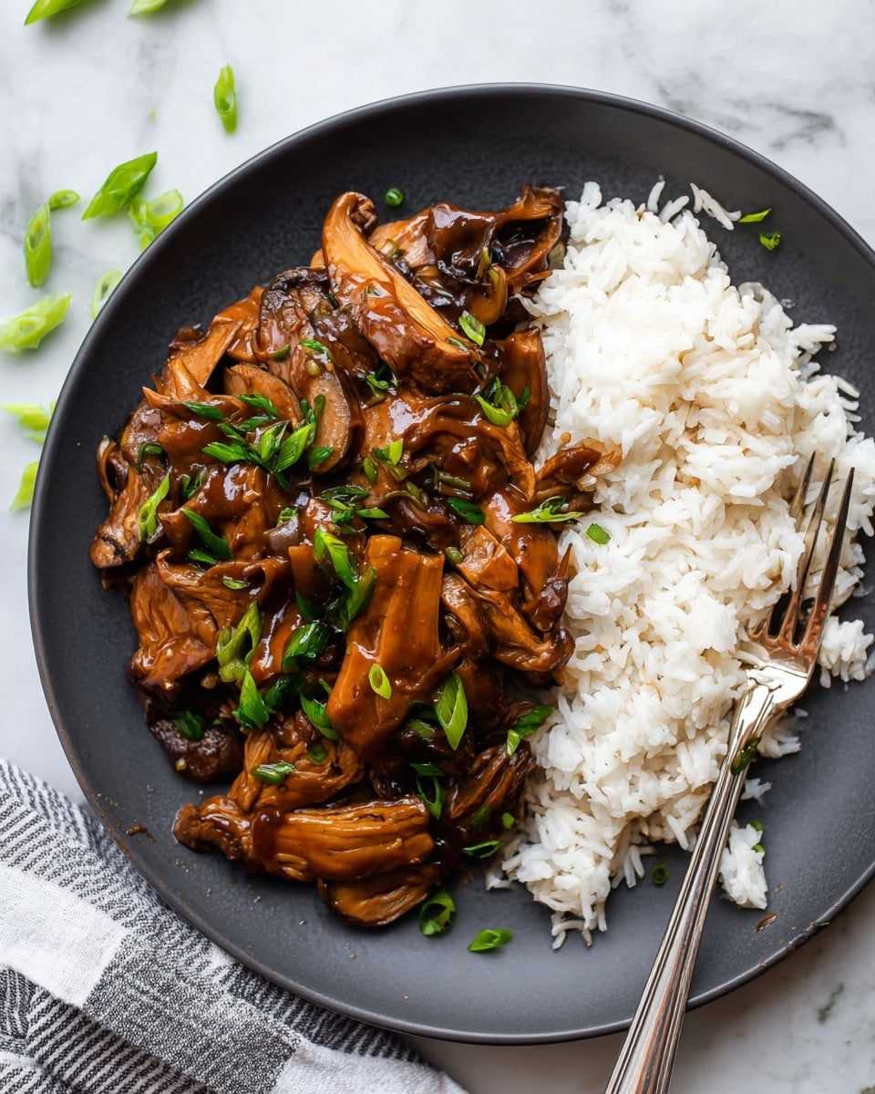 A dark gray plate holds a serving of white rice on the right side and a dark, glossy brown mushroom and vegetable stir-fry on the left side. The stir-fry consists of soft, thick mushroom pieces coated in a rich brown sauce, sprinkled with bright green sliced scallions. A silver fork lies on the right side, partially resting on the rice. The plate is set on a white marbled surface with a striped cloth napkin nearby and some green scallion pieces scattered at the top of the image. photo taken with an iphone --ar 4:5 --v 7