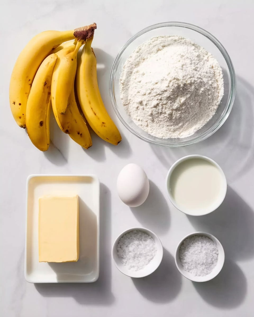 The image shows several ingredients arranged neatly on a white marbled surface. On the left, there are three yellow bananas with a few dark spots, lying close together. To their right, there is a clear glass bowl filled with white flour, showing a soft powdery texture. Above and slightly to the right of the flour bowl, there is a white bowl containing a smooth, thick white liquid. Below it and closer to the center of the image, there is a whole white egg. In front of the egg and slightly to the left, a white rectangular dish holds a pale yellow stick of butter. On the right side, there are three small white bowls lined up vertically, each holding a different white powder or crystalline substance, with varying textures from fine powder to small crystals. The layout is clean and bright, with all items placed on a white marbled surface, and soft natural lighting coming from above. photo taken with an iphone --ar 4:5 --v 7