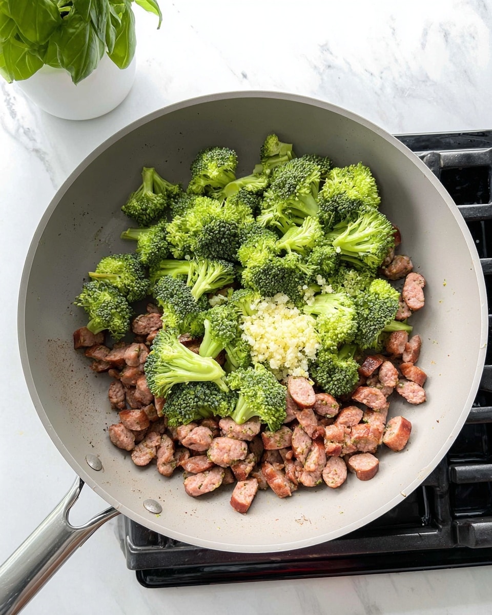 In a light gray pan on a black stove, there are small pieces of cooked sausage that are brown with a slight shine, spread across the bottom. On top of the sausage, there are fresh green broccoli pieces with a rough texture, and in the center, a small mound of minced or crushed garlic shows a pale yellow color. The background surface is a white marbled texture, and a green leafy plant in a white pot sits to the side. Photo taken with an iphone --ar 4:5 --v 7