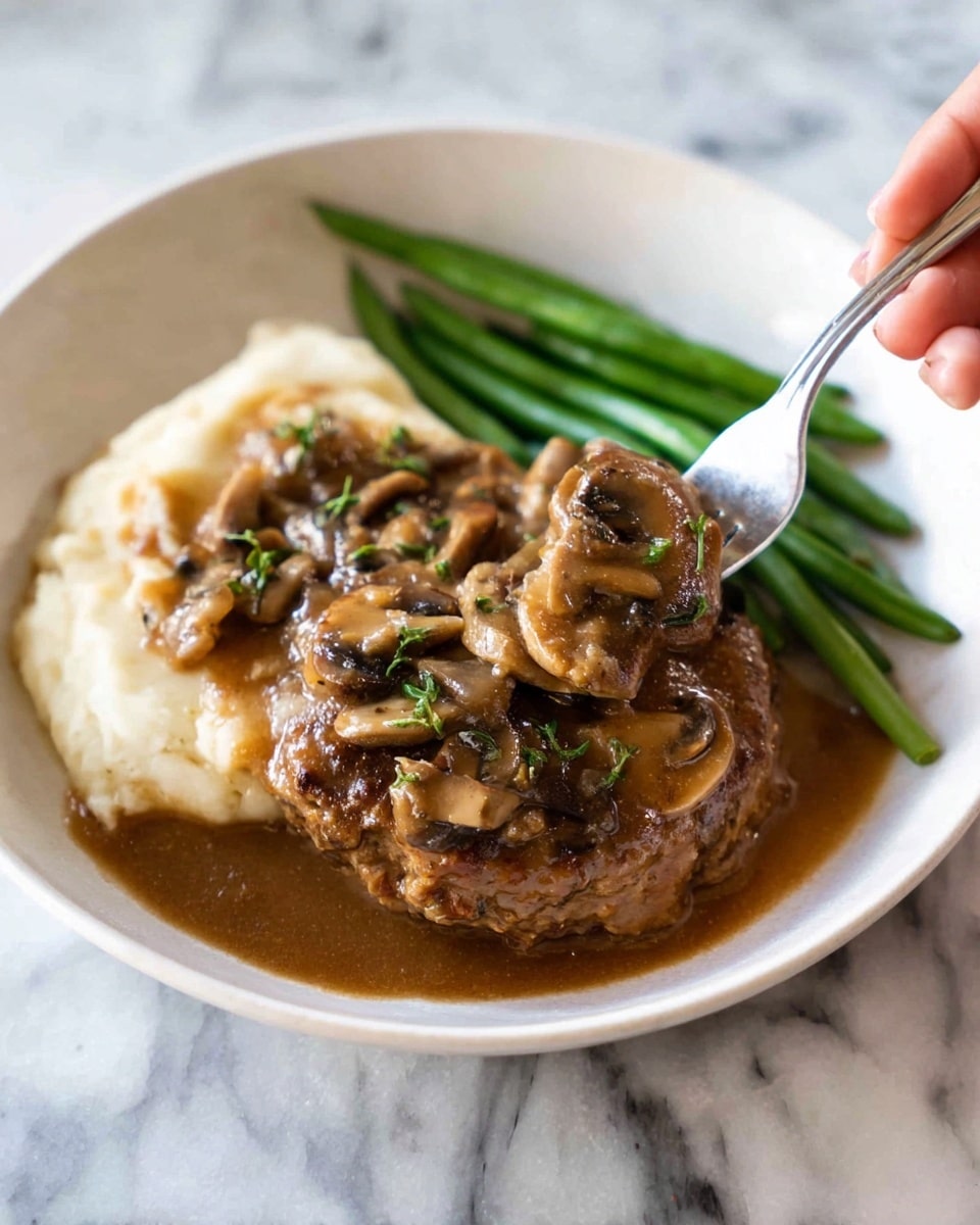 A white plate holds three main parts: on the left, a base layer of smooth, creamy white mashed potatoes; in the center, a thick, browned meat patty covered with glossy brown mushroom gravy, with sliced mushrooms and small green herb pieces on top; on the right, a neat pile of bright green beans with a slight shine. A silver fork, held by a woman's hand, is lifting a small piece of the meat patty. The plate sits on a white marbled surface. photo taken with an iphone --ar 4:5 --v 7