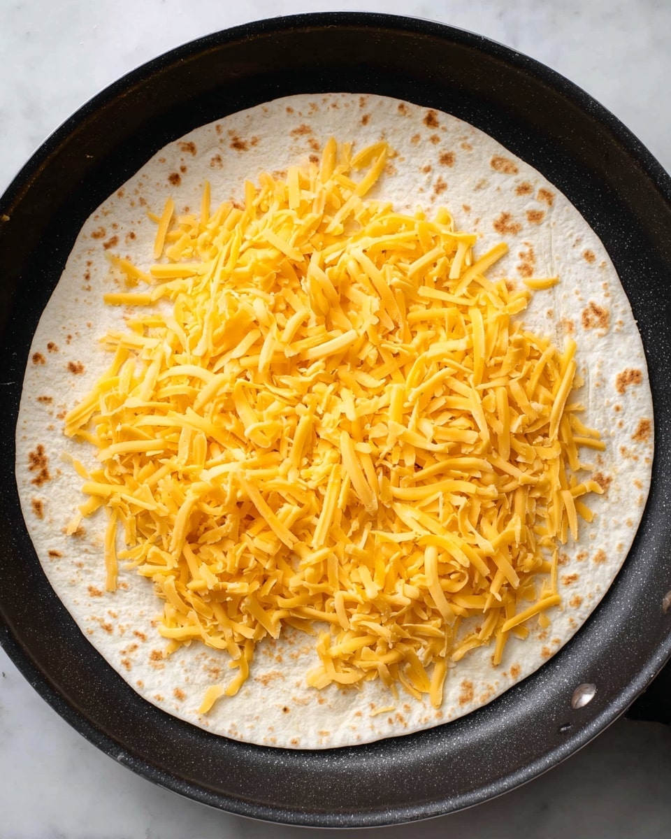 A thin white tortilla lays flat in a black pan, covering the bottom almost fully. On top of the tortilla is a single even layer of shredded bright orange cheese scattered widely but not clumped, with some patches of the tortilla visible underneath. The pan's dark texture contrasts with the tortilla's pale, slightly toasted spots. The setting is on a white marbled surface, giving a clean and simple background. photo taken with an iphone --ar 4:5 --v 7