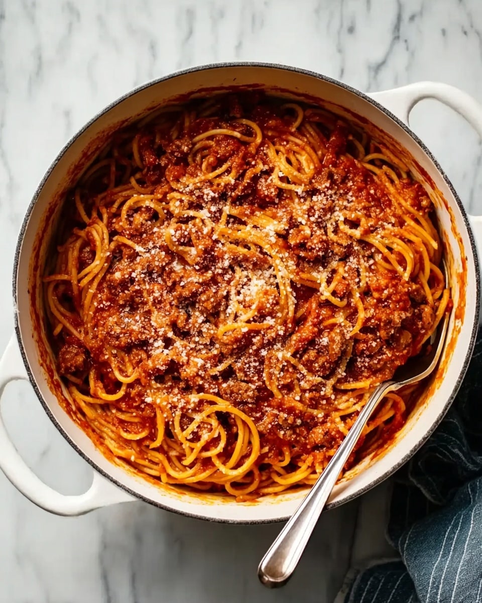 A white pot filled with spaghetti pasta covered in thick, red tomato sauce mixed with small pieces of browned meat. The sauce looks rich and chunky, with some pasta strands visible on top, twisting through the sauce. A sprinkling of grated cheese lightly covers the sauce, adding a touch of white and texture contrast. The pot sits on a white marbled surface with a long-handled pasta fork placed nearby. photo taken with an iphone --ar 4:5 --v 7