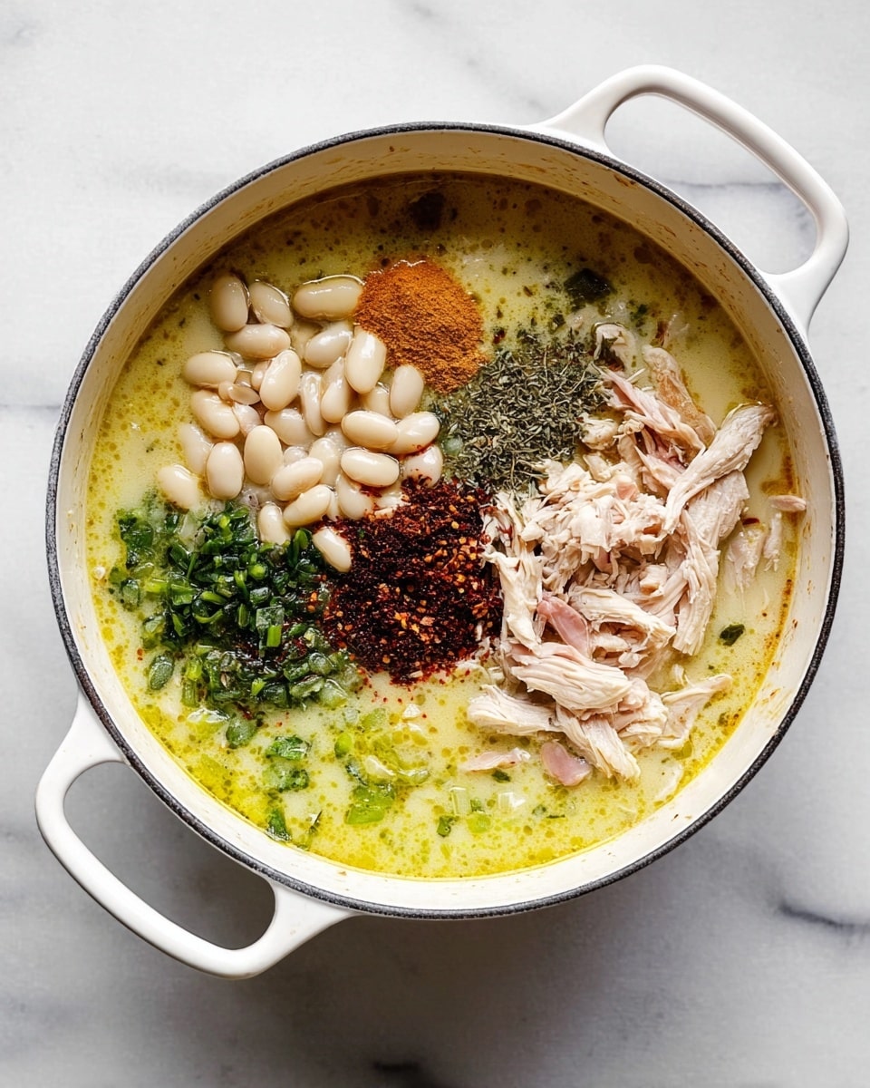 A white pot filled with a creamy yellow broth as the base layer, with small pieces of green herbs floating on the surface. On top of the broth are several clusters of ingredients spread around: a pile of white beans, shredded pale pink chicken, green chopped vegetables, and a mix of dry spices that include dark brown, red, and green powders. The pot is set on a white marbled surface, and its white handles are visible on the left and right sides of the image. photo taken with an iphone --ar 4:5 --v 7