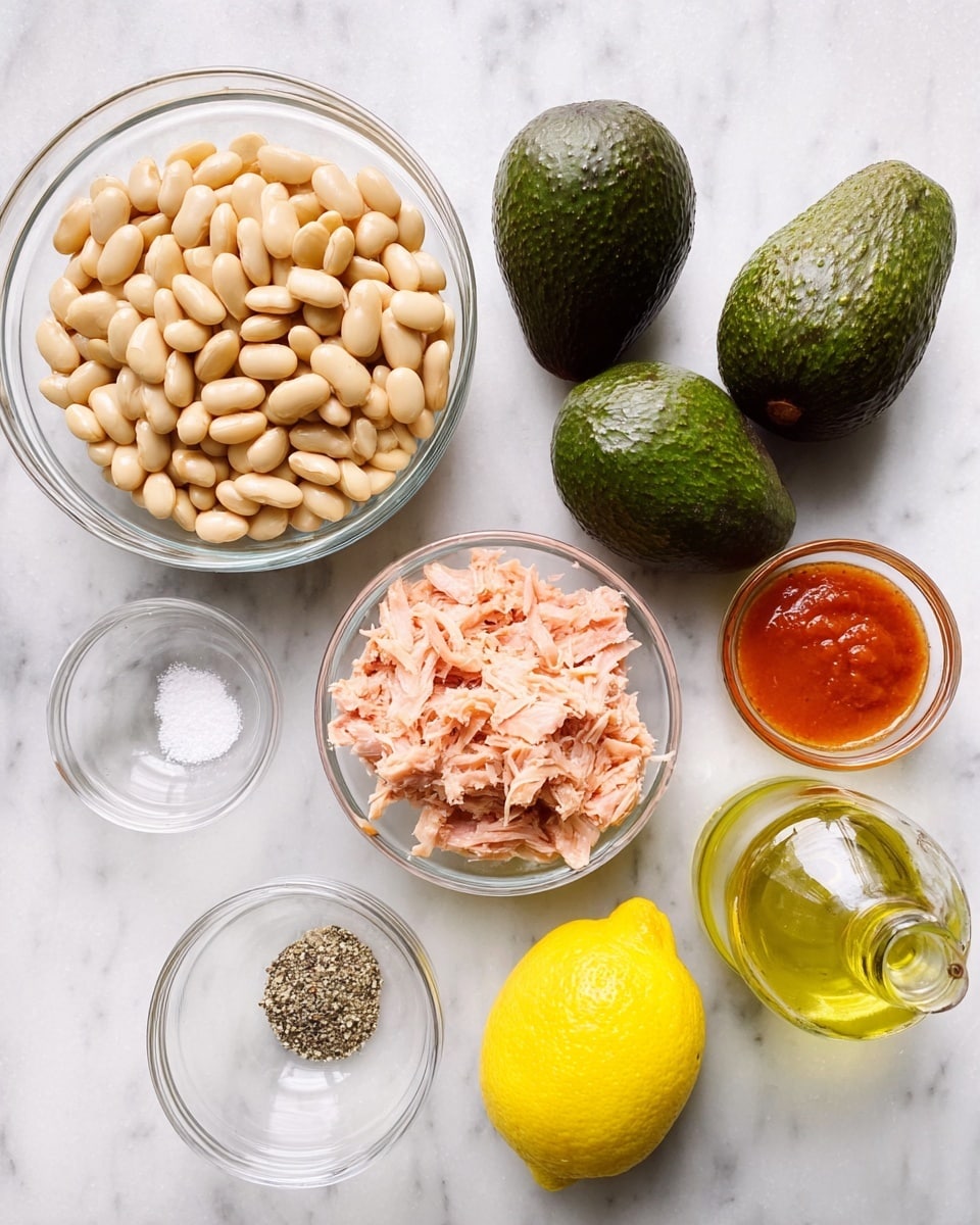 The image shows seven ingredients placed on a white marbled surface in clear glass bowls and loose. Starting from the top left, there is a large bowl filled with pale beige cannellini beans, smooth and slightly shiny. To the right of the beans are two whole dark green avocados with textured skin, side by side. Below the avocados, on the right side, is a medium bowl filled with shredded light pink tuna. Below the beans, towards the bottom left, is a small bowl containing a mix of white salt and black pepper. Next to it is a whole bright yellow lemon with a smooth skin. To the right of the lemon is a small bottle filled with light yellow olive oil. Above the bottle and lemon, in the center, is a small bowl with orange-red hot sauce. Photo taken with an iphone --ar 4:5 --v 7