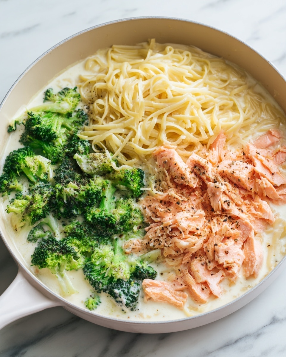 A white pan filled with three layers of food is shown on a white marbled surface. The bottom layer is creamy white sauce that covers the entire pan. On top of this sauce, there is a layer of cooked light yellow noodles spread evenly across the pan. Next, the third layer consists of bright green broccoli pieces on one side and flaked pink cooked salmon on the other side. The salmon is seasoned with black pepper. In the last frame, the salmon, broccoli, and noodles are gently mixed together in the creamy sauce. Photo taken with an iphone --ar 4:5 --v 7