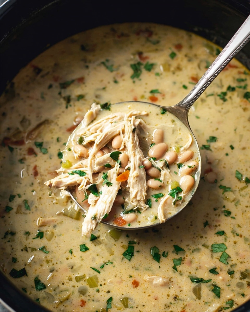 The image shows a close-up view of a creamy soup inside a black pot. The soup has a light beige color with visible pieces of shredded pale chicken, small orange beans, and diced light green celery. There are also scattered finely chopped green herbs throughout the soup. A silver ladle is scooping some soup, showing the mix of chicken, beans, celery, and herbs clearly. The white marbled background is partially visible around the pot edge. photo taken with an iphone --ar 4:5 --v 7