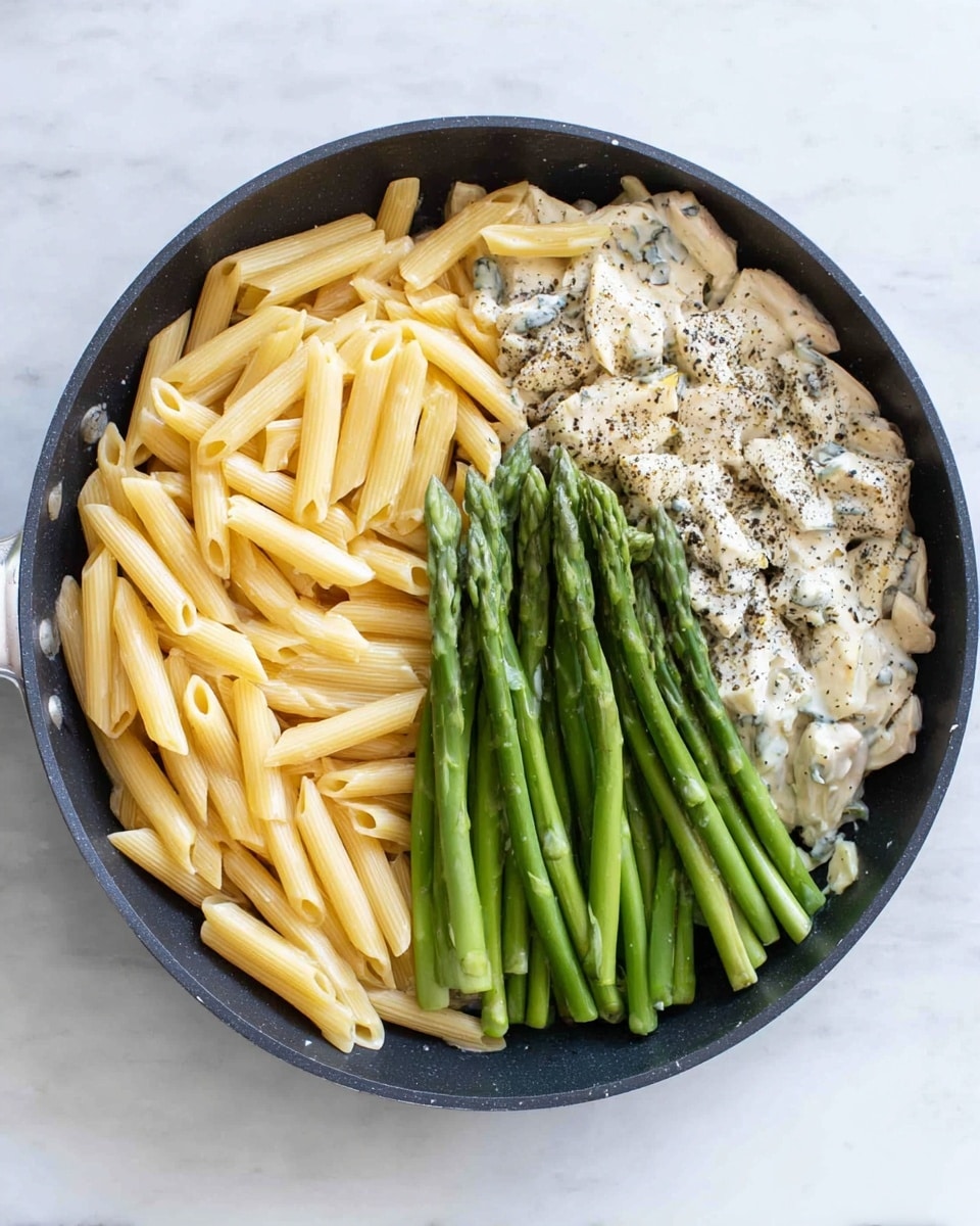 A black pan with three main sections of food placed separately inside it is shown from above. On the left side there is a pile of cooked pale yellow penne pasta, its texture smooth and tubular. At the bottom right, a cluster of bright green asparagus stalks with a firm, fresh appearance sit in a group arranged diagonally. On the top right is a creamy white chicken and sauce mix, speckled with black pepper giving it a slightly grainy look, spread flat against the pan’s surface. All elements are arranged side by side, not mixed, on a white marbled surface photo taken with an iphone --ar 4:5 --v 7