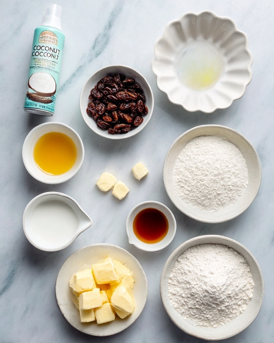 The image shows eight cooking ingredients arranged neatly on a white marbled surface. In the top left corner, there is a light blue and white can of coconut oil cooking spray. Moving clockwise, there is a small white bowl with a yellow liquid, a scalloped white bowl filled with dark brown raisins, and a small white bowl holding a dark amber liquid. Below this, there is a white measuring cup filled with a white liquid, a white plate with small piles of white powdery substances, a white bowl with yellow butter cubes, and two medium white bowls filled with two different types of white flours, one with a slightly coarser texture and the other finer. The overall setup is clean and bright, photo taken with an iphone --ar 4:5 --v 7