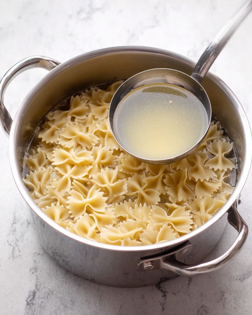 A shiny silver pot filled with light yellow bow-tie pasta in water sits on a white marbled surface. Above the pot, a silver ladle holds a small amount of cloudy, pale yellow pasta water, about to be poured into the pot. The shapes of the pasta are clearly visible, showing soft edges and a slightly wet texture. The pot has two handles on each side with shiny reflections. photo taken with an iphone --ar 4:5 --v 7