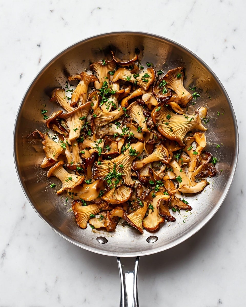 The image shows a silver frying pan filled with cooked oyster mushrooms in one layer. The mushrooms have a golden-brown color with some darker crisp edges, and their texture looks soft with slight wrinkles. There are small green parsley pieces sprinkled over the mushrooms, adding a fresh touch. The pan has a shiny metal handle pointing downward, and the whole scene is set on a white marbled surface. photo taken with an iphone --ar 4:5 --v 7