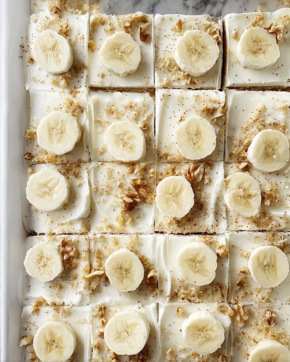 The image shows a white rectangular pan filled with twenty pieces of cake arranged in four rows and five columns, each square topped with a smooth, thick white frosting layer. On top of each piece are light beige banana slices placed mostly in pairs, along with small bits of crushed walnuts scattered evenly across all the pieces, adding texture and a speckled pattern on the white frosting. The cake surface is creamy and slightly uneven, with edges between pieces clearly visible. The background is a white marbled surface. photo taken with an iphone --ar 4:5 --v 7