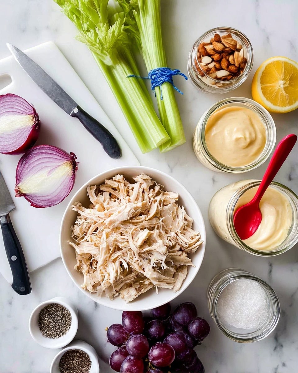 The image shows a white bowl in the center filled with shredded light brown cooked chicken on a white marbled surface. To the left of the bowl is a white cutting board holding two halves of a red onion and a black-handled knife. Above the bowl is a bundle of green celery sticks tied with blue string. To the right of the bowl is a glass jar of creamy pale yellow mayonnaise with a red spoon inside. Next to the jar are two halves of a bright yellow lemon. Below the lemon is a bunch of dark purple grapes. Near the grapes are two small white bowls, one filled with black pepper and the other with white salt. A glass jar with sliced almonds inside is near the top left of the frame. photo taken with an iphone --ar 4:5 --v 7