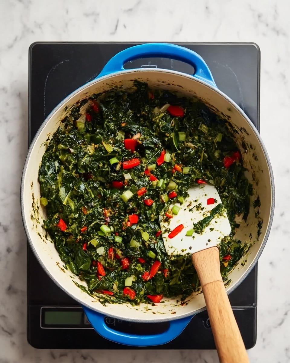 A top view of a blue handled white pot filled with a mix of dark green chopped spinach leaves, small pieces of bright red bell pepper, and some light green chopped scallions, all cooked together. A white spatula with a wooden handle is resting inside the pot on the right side, partially covered in the green spinach mix. The pot is set on a black digital stove, which sits on a white marbled surface photo taken with an iphone --ar 4:5 --v 7