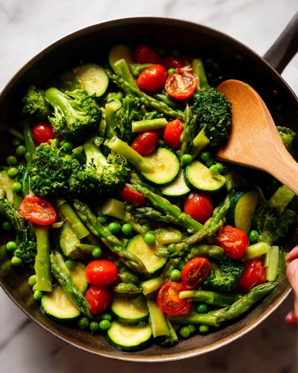 The image shows a pan full of cooked mixed vegetables, mainly green in color with some bright red accents. The vegetables include green broccoli florets with a rough texture, smooth round slices of zucchini layered throughout, and light green asparagus spears cut diagonally. Small round green peas are scattered around, adding a tiny pop to the mix. Bright red cherry tomatoes, some whole and some slightly softened and split, are mixed in evenly, creating contrast among the greens. A wooden spoon rests on the right side of the pan, with a woman's hand holding it gently as if stirring the vegetables. The background surface is a white marbled texture. photo taken with an iphone --ar 4:5 --v 7