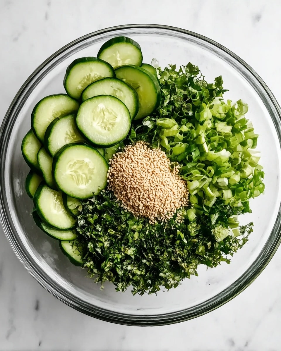 A clear glass bowl sits on a white marbled surface filled with fresh ingredients arranged in layers. On one side, thinly sliced green cucumbers create a neat semi-circle, their light green color contrasting with darker green herbs next to them. A pile of light green chopped scallions lies opposite the cucumbers, and in the center, a small mound of light tan sesame seeds is placed on top of finely chopped dark green herbs, creating texture variety. The overall look is fresh and vibrant with different shades of green and the contrasting sesame seeds. photo taken with an iphone --ar 4:5 --v 7