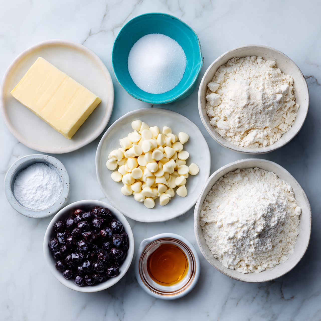 The image shows seven small bowls and plates arranged on a white marbled surface, each containing a different ingredient. On the left is a white plate with a stick of pale yellow butter. Above it, there is a turquoise bowl filled with white granulated sugar. To the right of that is a small white plate holding two small piles of white powder, likely baking powder and baking soda. Above this plate, a white bowl is filled with white chocolate chips. Next to it on the right, a larger white bowl holds a pile of white flour. Below the flour to the right, a white ramekin contains dark purple frozen blueberries. In the center bottom is a small glass bowl with a small amount of amber-colored liquid, probably vanilla extract. Everything is cleanly arranged and well-lit. photo taken with an iphone --ar 4:5 --v 7