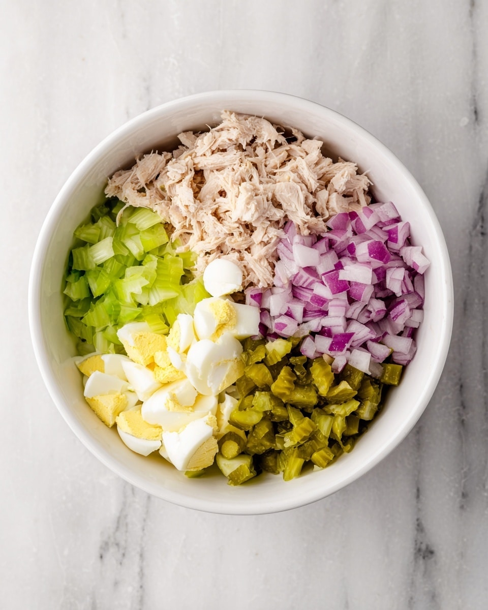 A white bowl sits on a white marbled surface filled with five sections of ingredients, each taking up about one-fifth of the bowl's space. In the top left is light tan shredded chicken with a soft, flaky texture. To its right is finely chopped purple onions with sharp edges. Next to the onions is bright green chopped pickles with a slightly wet look. Below the pickles is pale yellow and white hard-boiled eggs, chopped into chunks with a firm texture. Finally, at the bottom left is light green chopped celery, crisp and fresh in appearance. photo taken with an iphone --ar 4:5 --v 7